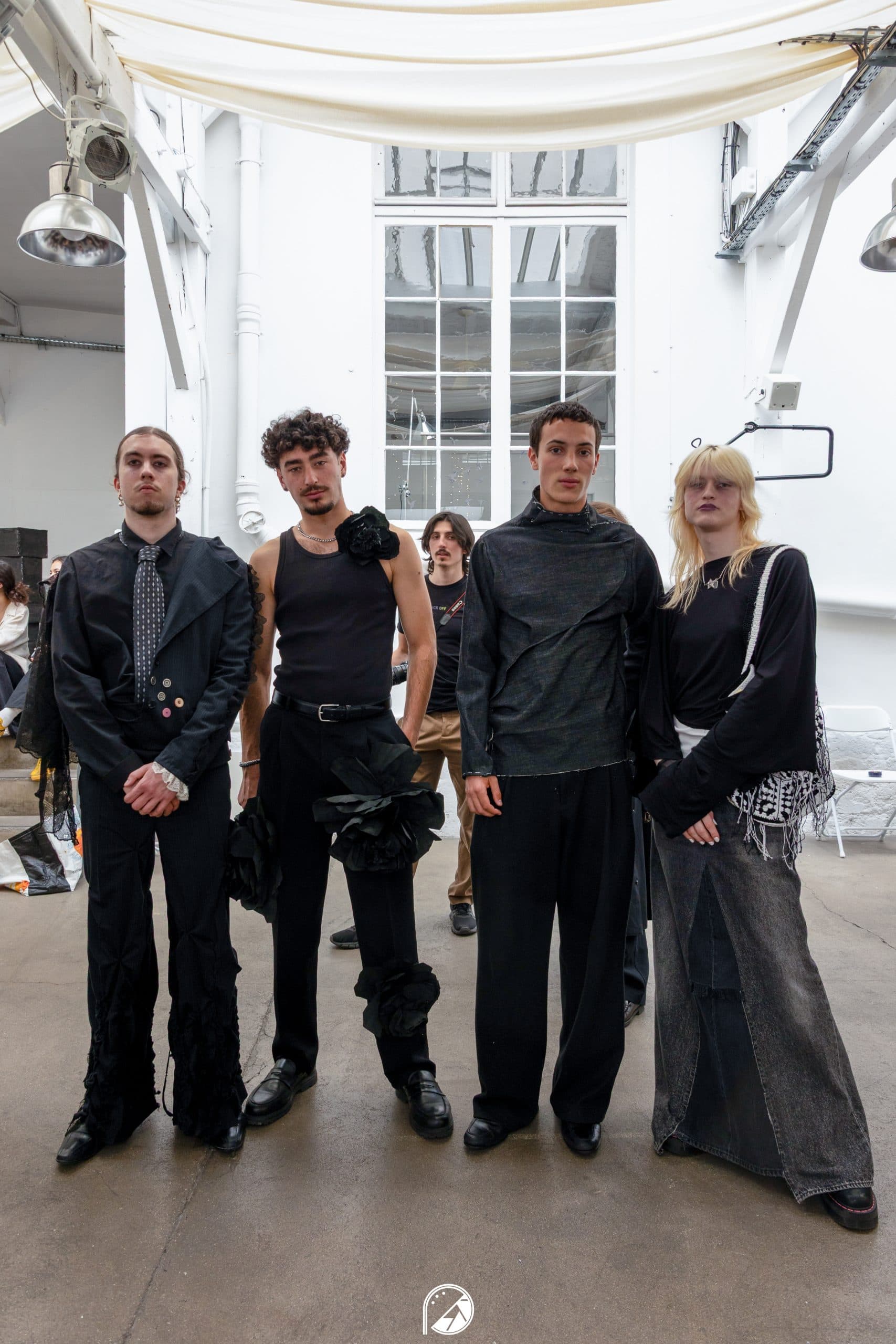 Four models in deconstructed all-black looks standing under the glass roof of Le QG