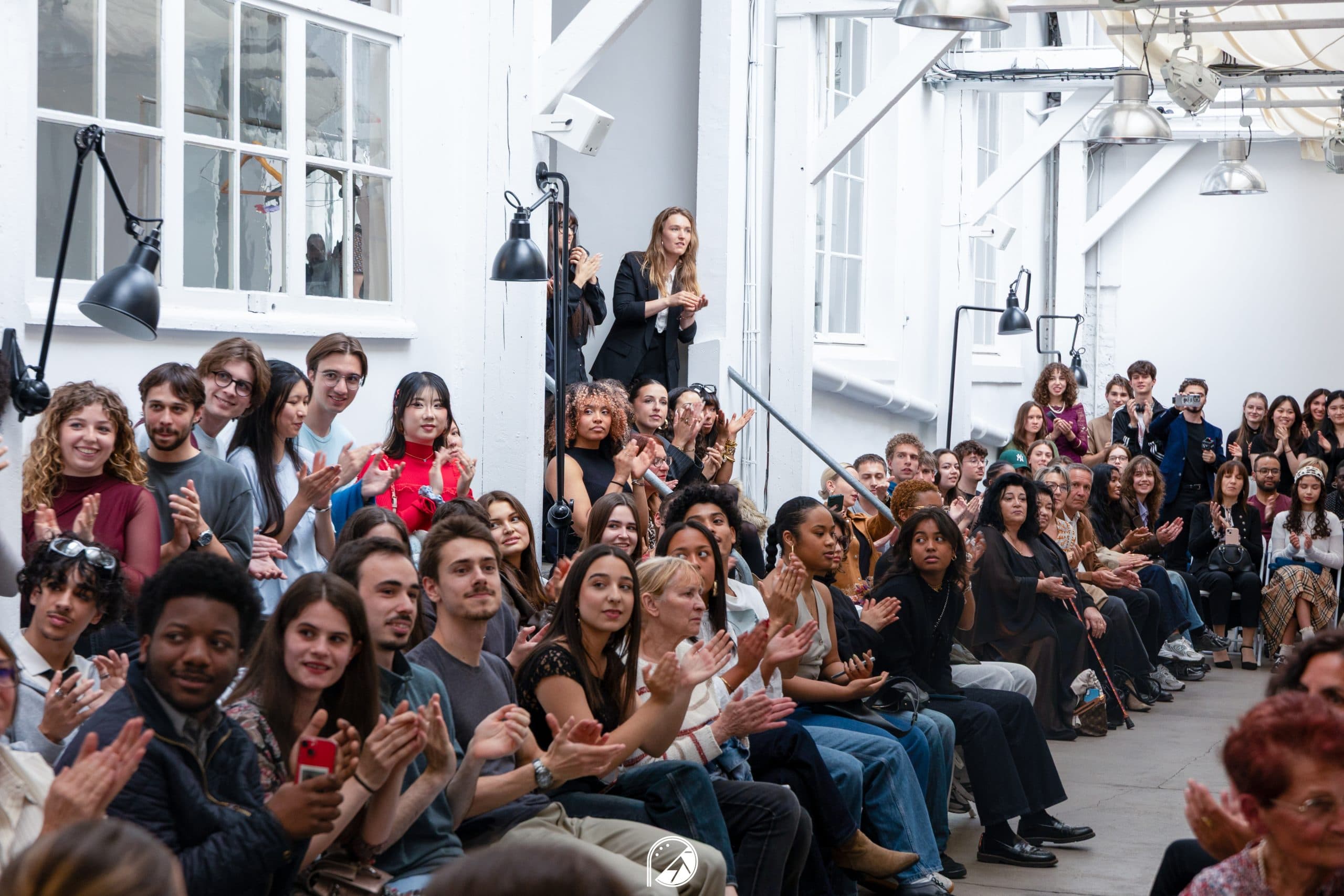 Audience applauding along the runway inside the white industrial venue
