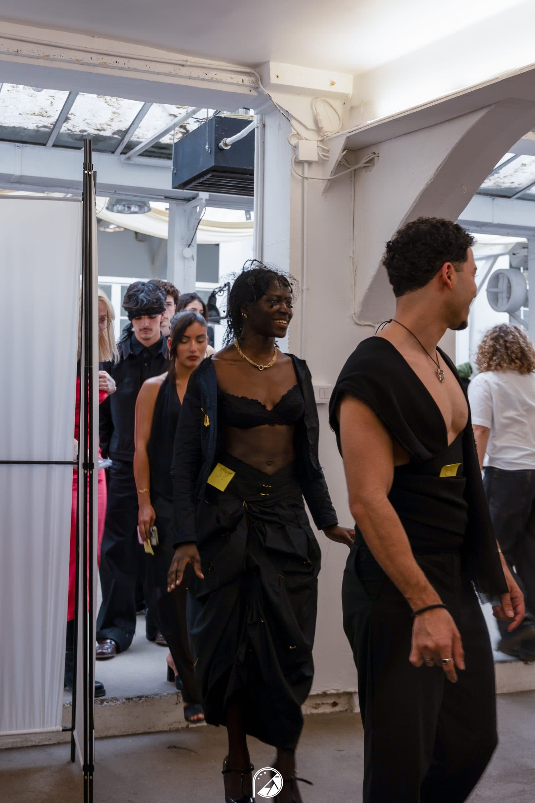 All-black silhouettes with numbered tags walking in order from backstage toward the runway