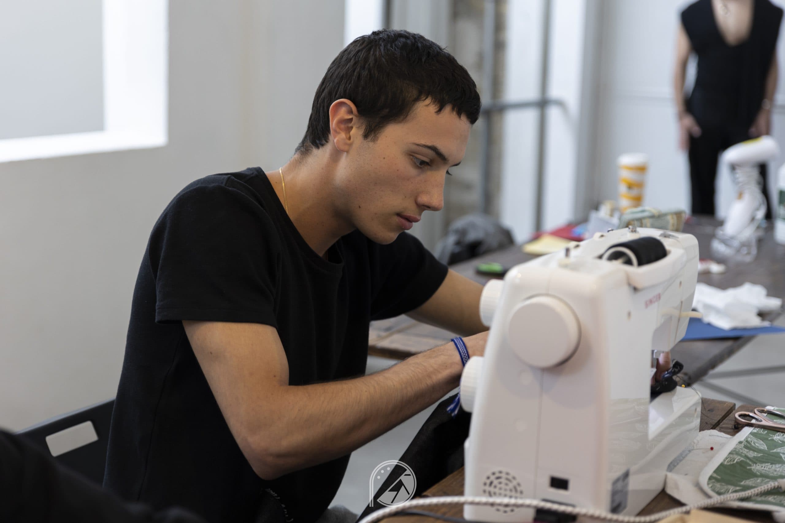 A team member sewing a black garment on a sewing machine backstage