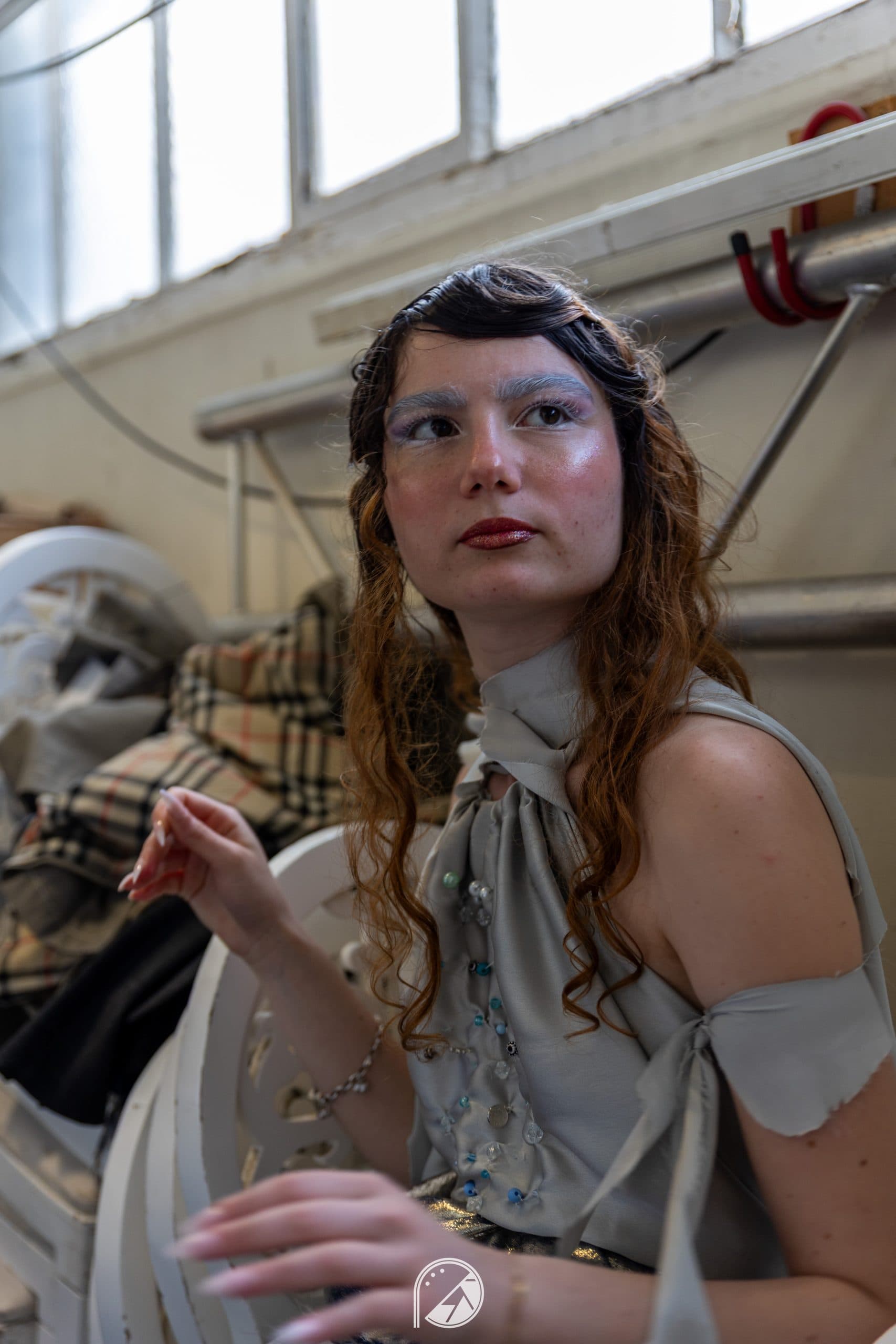 Close-up of a model backstage with bleached, textured eyebrows, glossy skin and red lips
