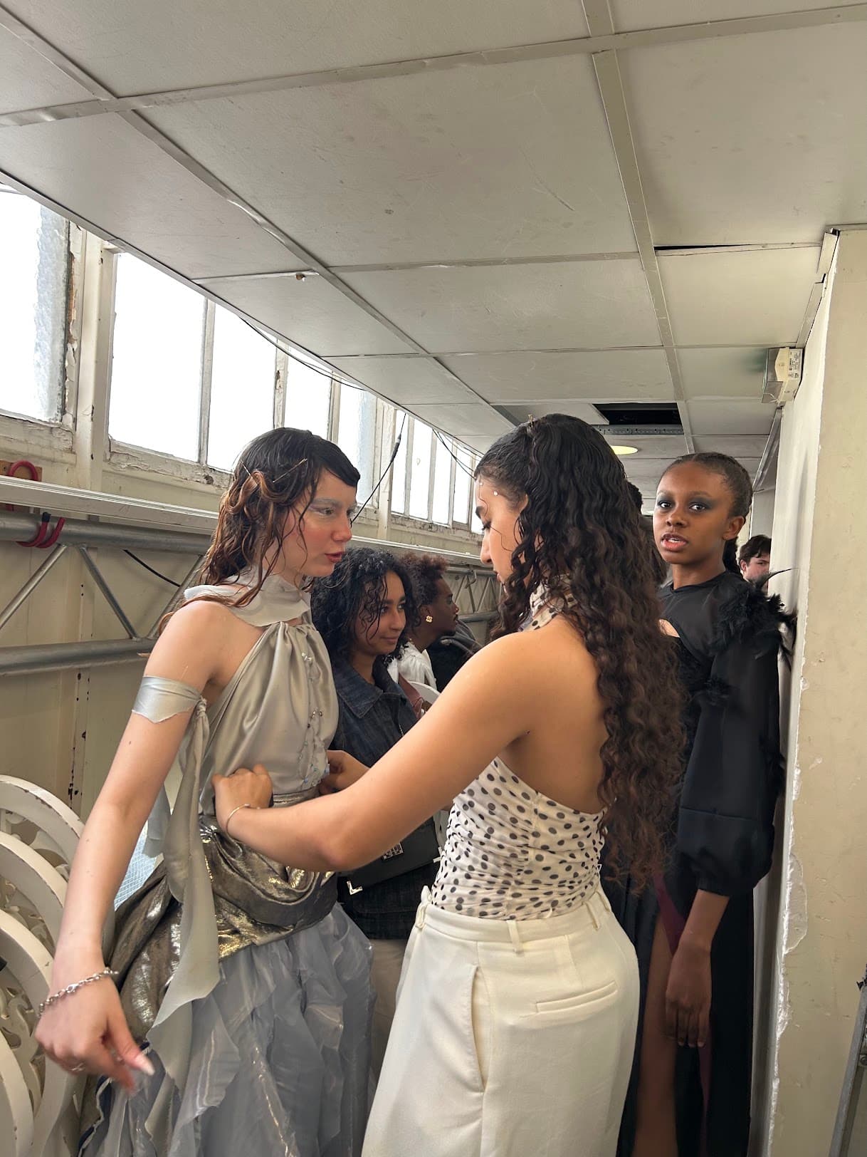 Adjusting the silver draped bodice of a gown backstage before the show