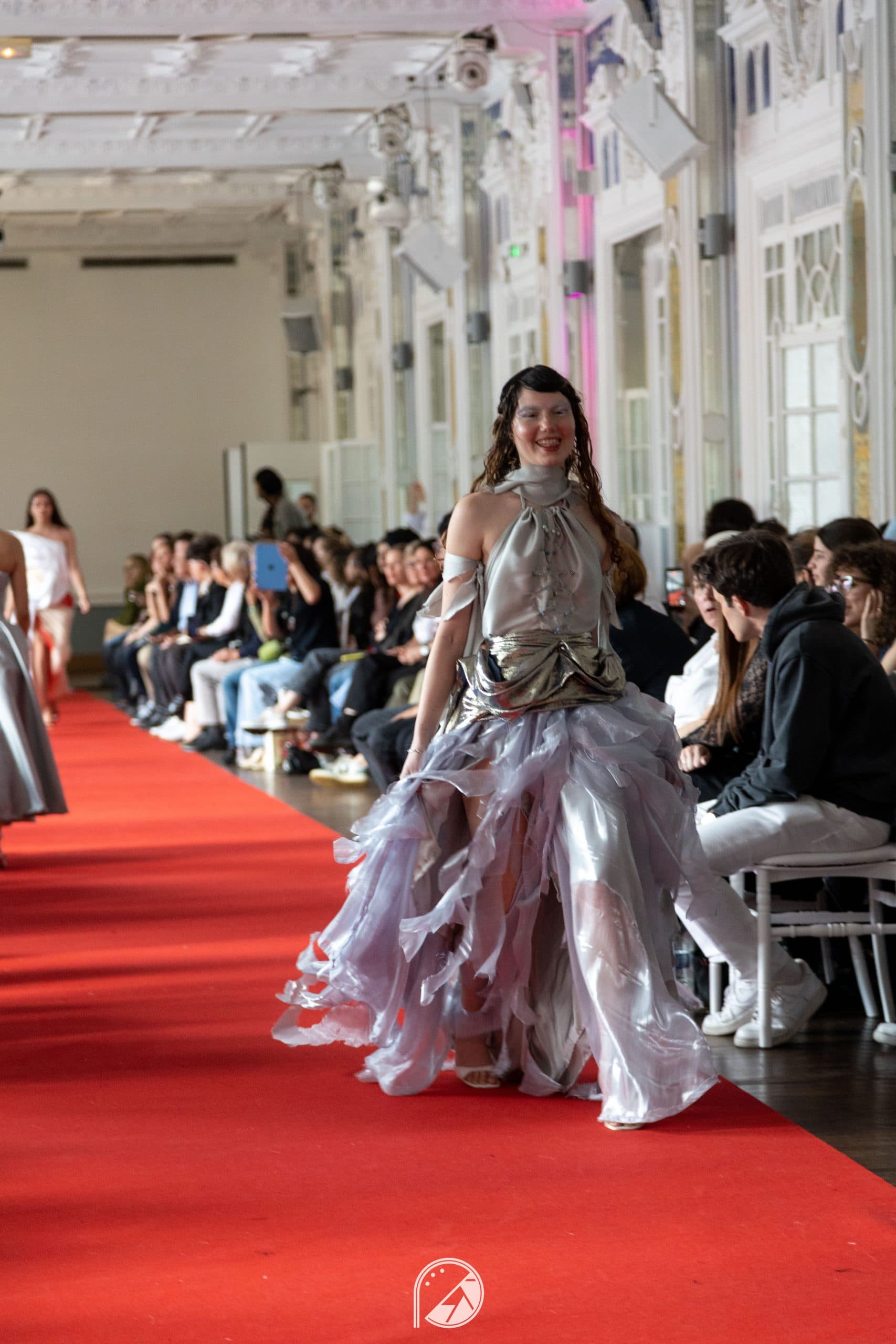 The silver and lilac organza gown in motion on the red carpet, the audience seated along the mirrored walls