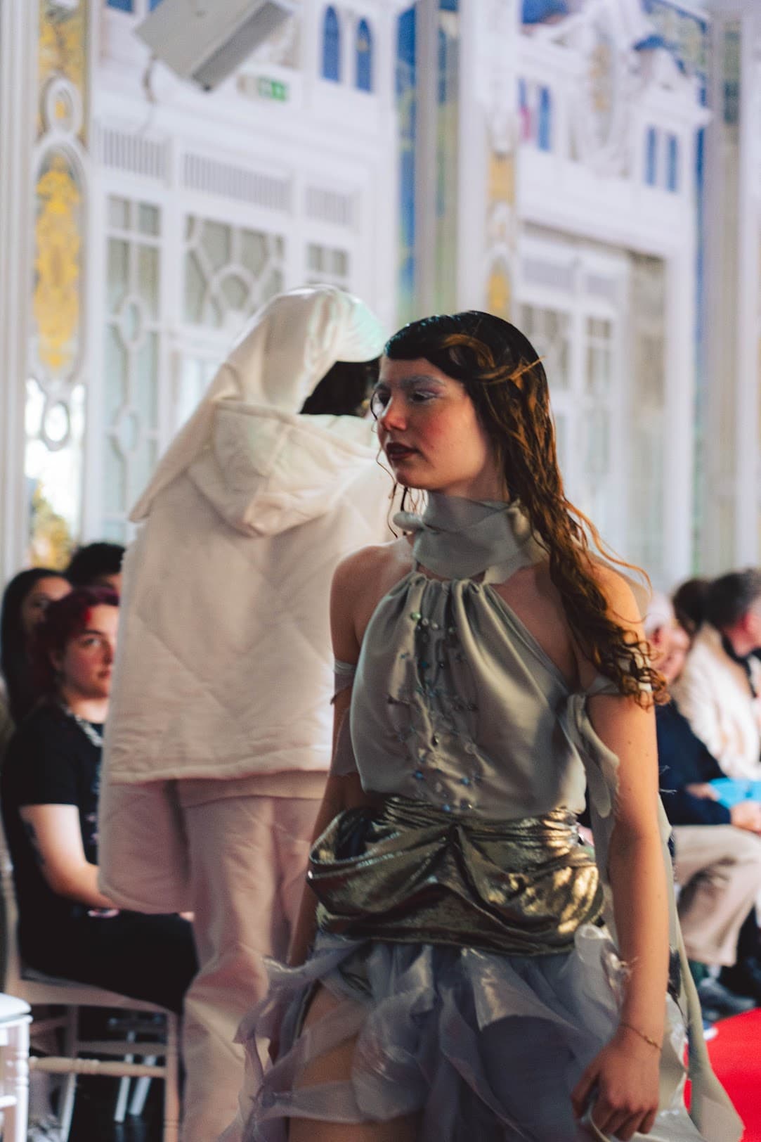 The model in the silver gown walking past the audience, painted mirrored walls behind her