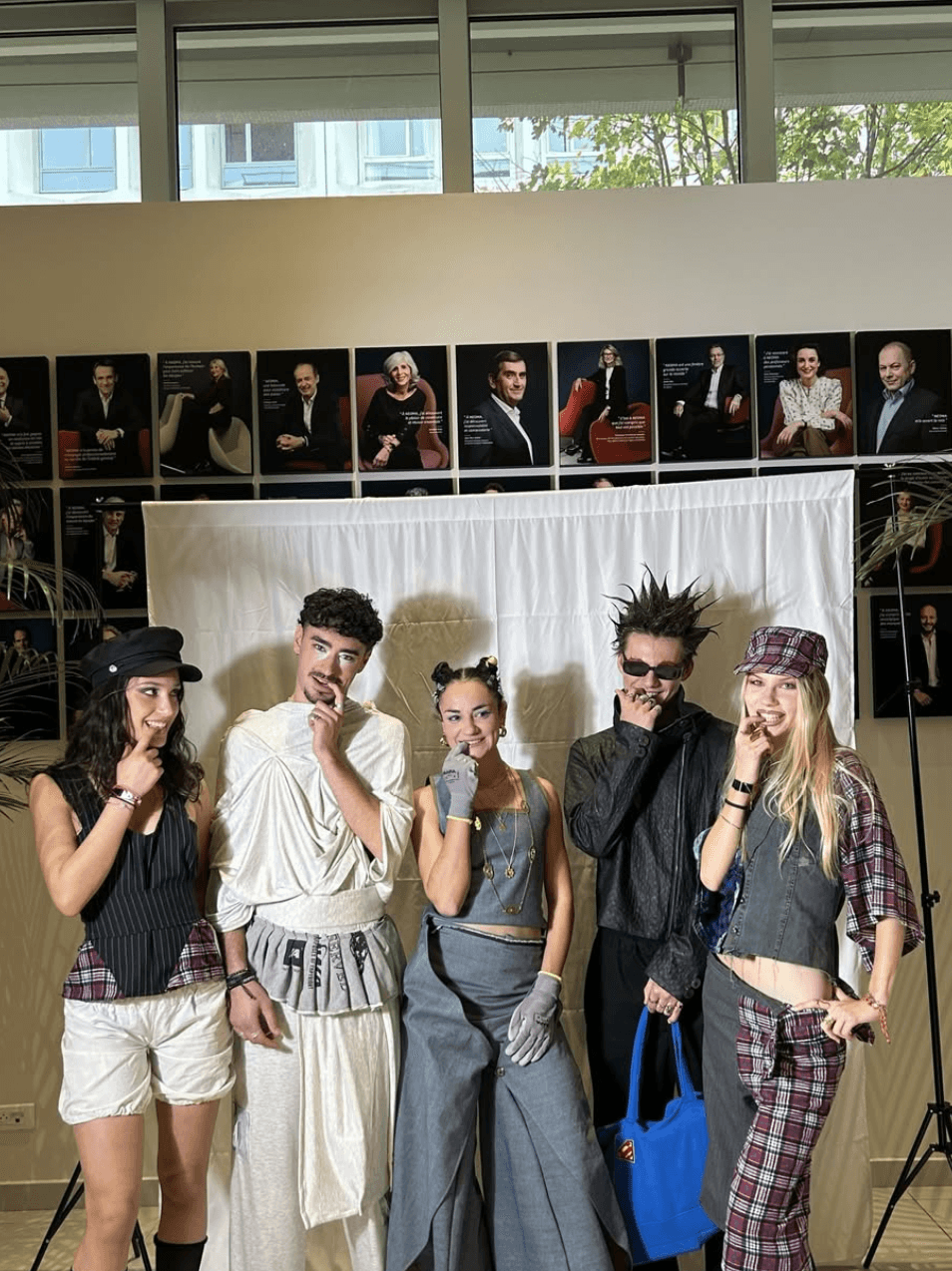 Five models in pinstripe, plaid, denim and draped looks posing in front of a white backdrop